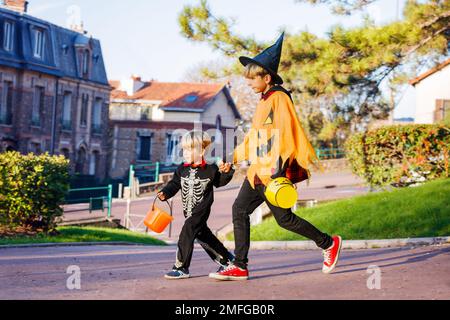 Zwei Jungs gehen in Halloween-Kostümen mit Süßigkeiten-Eimern über der Stadt Stockfoto