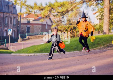 Zwei Brüder laufen in Halloween-Kostümen und halten Süßigkeiten-Eimer Stockfoto