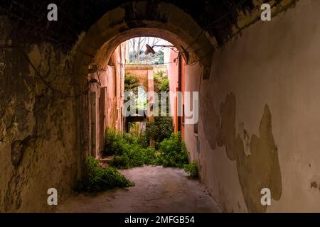 Eine kleine, zerstörte Gasse mit Torbögen, Steinmauern und überwucherten Treppen im alten Teil der Stadt Ragusa. Stockfoto