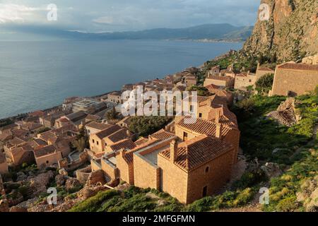 Blick auf das befestigte mittelalterliche Schlossdorf Monemvasia mit dem Ägäischen Meer und der Küste von Lakonia als Hintergrund. Steinhäuser mit staubigen rosa Terrakotta-Fliesen Stockfoto