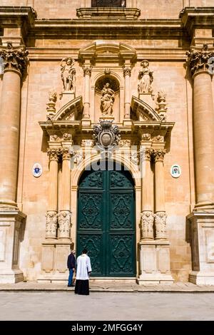 Ein Priester nähert sich dem westlichen Eingang der Kirche Ragusa Kathedrale, Duomo di Ragusa, Cattedrale di San Giovanni Battista. Stockfoto