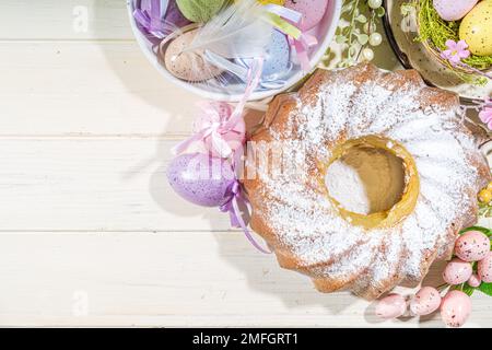 Traditionelle Frühlingsferien Osterrunde Kuchen mit Puderzucker gekrönt. Auf hellem Holzhintergrund mit Sonnenlicht, Ostereiern, Dekor und Frühlingszwirnholz Stockfoto