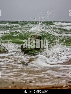 Ein vertikaler Langzeitaufnahme von Wellen, die an einem düsteren Tag in die Steingärten der Ostsee stürzen Stockfoto