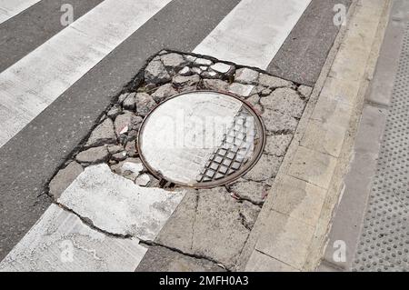 Große Grube mit Steinen auf der Asphaltstraße mit alter kaputter Schachtabdeckung Stockfoto