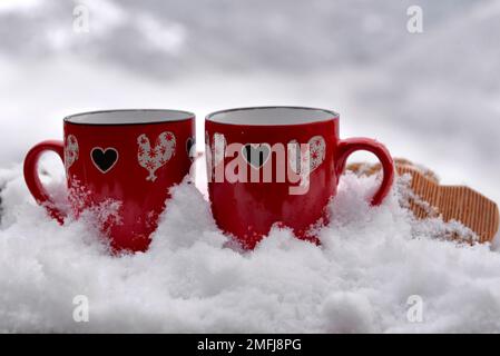 Zwei rote Tassen mit Herzform auf dem schneebedeckten valentinskonzept Stockfoto