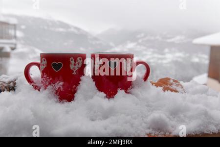 Zwei rote Tassen mit Herzform im Schnee- und Berghintergrund - valentinskonzept Stockfoto