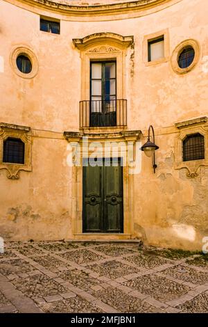 Fassade eines Hauses mit Eingangstür und Balkon in einem Innenhof in der spätbarocken Stadt Noto. Stockfoto