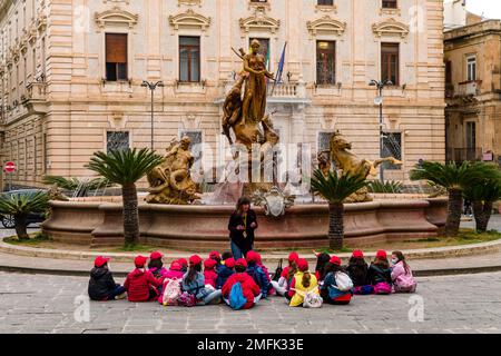 Schulkinder sitzen am kunstvollen Brunnen Fontana di Diana auf der Piazza Archimede, der 1878 in der späten barocken Stadt Syrakus erbaut wurde. Stockfoto