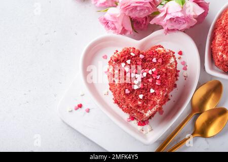 Zwei Kuchen Roter Samt in Form von Herzen auf weißem Teller, Rosenblumen und eine Tasse Kaffee auf rosafarbenem romantischem Hintergrund. Dessert-Idee für den Valentinstag, Stockfoto