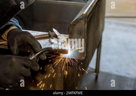 Ein Argon-Gas-geschirmtes Lichtbogenschweißgerät wird von Arbeitern verwendet, um Metall mit Funken auf halbautomatischen Schweißgeräten zu schweißen Stockfoto