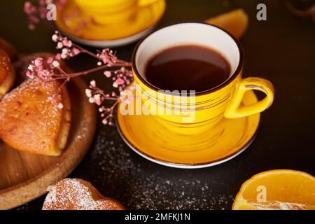 Gelbe Tassen, Teezeit und hausgemachte herzförmige Muffins. Cupcakes mit Orangengeschmack zum Valentinsfrühstück Stockfoto