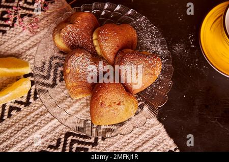 Hausgemachte herzförmige Cupcakes mit Orangengeschmack zum Valentinstag. Teezeit-Ästhetik mit frischen Muffins. Stockfoto