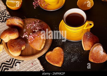 Ästhetische Teezeit mit gelben Tassen und hausgemachten herzförmigen Muffins. Cupcakes mit Orangengeschmack zum Valentinsfrühstück Stockfoto