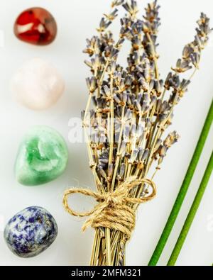 Erholende, energiereifende Zusammensetzung mit Lavendelblumen, Aromasticks und Chakrasteinen auf weißem Hintergrund. Konzept der Entspannung, Selbstpflege, medi Stockfoto