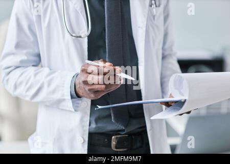 Nahaufnahme eines afroamerikanischen Arztes, der ein Klemmbrett hält, mit Patientenakte in der Klinik, Kopierraum Stockfoto