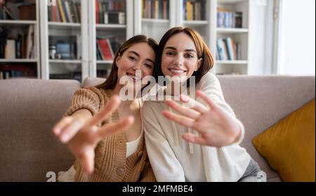 Fröhliche europäische Millennials-Freundinnen in Pullover machen Selfie für Blogs und soziale Medien, winken Hand Stockfoto
