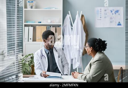 Seitenbild eines jungen schwarzen Arztes, der in der Klinik einen Patienten aufsucht und glücklich lächelt Stockfoto