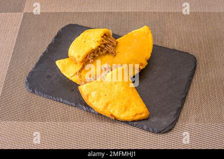 Köstliche Maismehl-Empanadas gefüllt mit geriebenem Fleischeintopf auf schwarzem Schieferteller Stockfoto