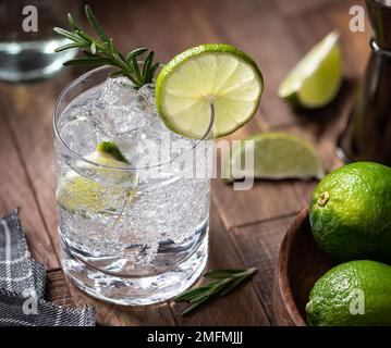 Gin und Tonic Cocktail mit Limettenscheiben, Rosmarin und Eis auf einem rustikalen Holztisch Stockfoto