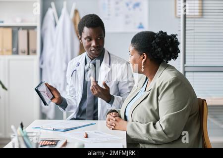 Seitenbild einer übergewichtigen schwarzen Frau, die Arzt in der Klinik hört Stockfoto