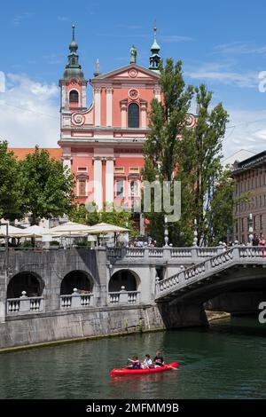 Ljubljana, Slowenien - 14. Juli 2022 - Menschen im Kajak auf dem Fluss Ljubljanica an der Dreifachbrücke und Franziskanerkirche der Verkündigung an der Preseren Squa Stockfoto