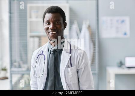 Klassisches Porträt eines jungen schwarzen Arztes, der vor der Kamera lächelt und einen Labormantel mit Stethoskop trägt Stockfoto