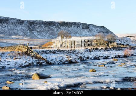 Die imposanten Felsen von Cronkley Fell und der alte Bauernhof des Wheysike House blickten über Harwood Beck vom Pennine Way im Winter, Forest-in-Teesd Stockfoto