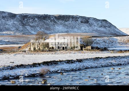 Die imposanten Felsen von Cronkley Fell und der alte Bauernhof des Wheysike House blickten über Harwood Beck vom Pennine Way im Winter, Forest-in-Teesd Stockfoto