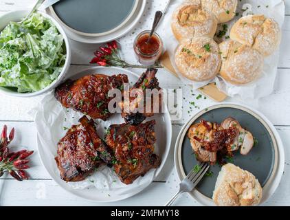 Dicke Schweinerippchen mit hausgemachter Barbecue-Sauce, Salat und Brotkranz. Köstliche Grillmahlzeit Stockfoto