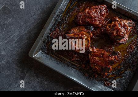 Dicke Schweinerippchen mit hausgemachter Barbecue-Sauce auf einem Backblech isoliert auf dunklem Hintergrund. Flach verlegt Stockfoto