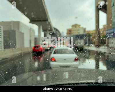 Selektive Fokussierung und Bewegungsunschärfe von Regentropfen auf der Windschutzscheibe eines Fahrzeugs in schwerem, langsam fahrendem Verkehr während eines Regengusses in Dubai vereinen Sie den Arabischen Emirat Stockfoto