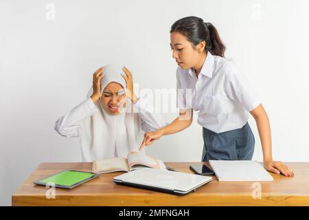 Zwei Highschool-Mädchen am Schreibtisch mit Büchern, während sie wütend waren Stockfoto