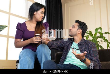 Glückliches, lächelndes junges Paar, das Tee oder Kaffee trinkt, während es sich zu Hause unterhält - Konzept von Familienurlaub, Paarbeziehung und Entspannung. Stockfoto