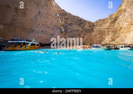 Wunderschöne Aussicht auf Boote, die Touristen zum alten rostigen Schiffswrack bringen, das am Strand von Navagio auf der Insel Zakynthos in Griechenland gestrandet ist, umgeben von hohen Klippen Stockfoto