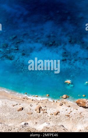 Wunderschönes kristallklares, blaues und türkisfarbenes Wasser neben einem Sandstrand mit großen Steinen in Myzithres, Zakynthos, Griechenland Stockfoto