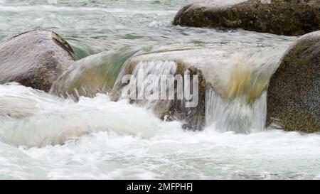 Das Wasser strömt über die Felsen des Flusses, während das saubere Wildwasser in den schnell fließenden Fluss fließt Stockfoto