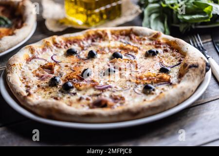 Italienische Speck-Pizza mit Zwiebeln und schwarzen Oliven auf weißem Teller. Stockfoto