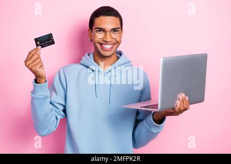 Foto eines jungen, lustigen, aufgeregten Promoter, Fernarbeiter, der eine Kreditkarte hat, Laptop bezahlt keine Steuern, freiberuflicher Job isoliert auf pinkfarbenem Hintergrund Stockfoto