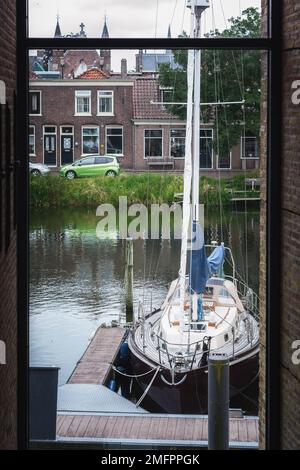 Blick aus dem Fenster auf einem verankerten Segelboot auf dem Pier im Zentrum von Enkhuizen. Stockfoto