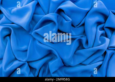 Die Textur eines glatten, luxuriösen, eleganten Stoffes in Blau. Stoff aus blauem Satin oder Seide mit Falten und Wellen Stockfoto