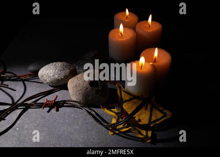 Holocaust-Gedächtnisfeiertag. Stacheldraht, Steine, gelber Stern und brennende Kerze auf schwarzem Hintergrund Stockfoto