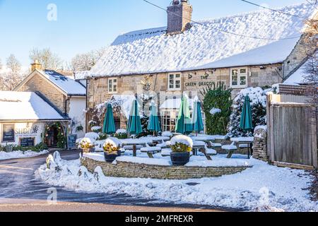 Frühwinterschnee im Green Dragon Inn Pub & Shop im Cotswold-Dorf Cockleford in der Nähe von Cowley, Gloucestershire, England Stockfoto