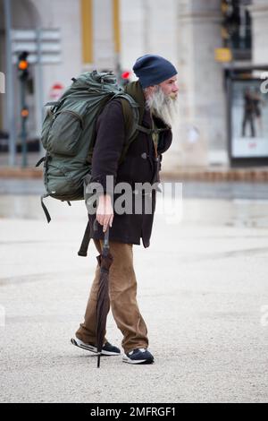 Ein Mann mit langem Bart in Winterkleidung und einem großen Rucksack, der durch die Straßen von Lissabon spaziert Stockfoto