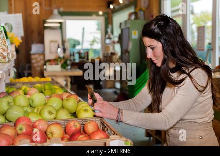 Eine Verkäuferin, die die Etiketten in einem Gemüsehändler anlegt - eine Verkäuferin, die in einem Supermarkt arbeitet - eine glückliche Frau ausgibt und arbeitet Stockfoto