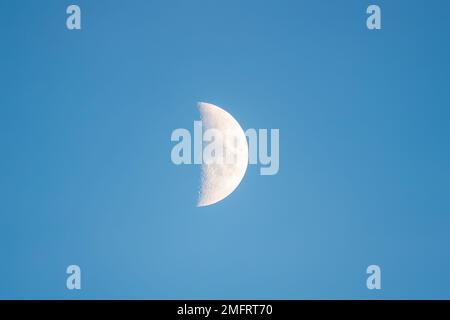 Ein halber Mond, von der Erde aus gesehen, mit blauem Hintergrund Stockfoto