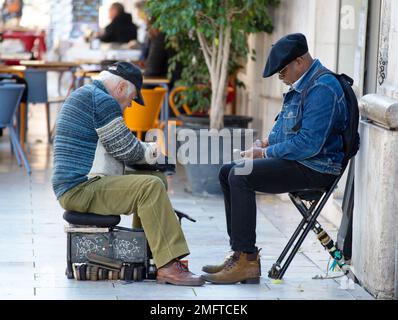 Ein älterer Mann putzt seine Schuhe auf der Straße Stockfoto