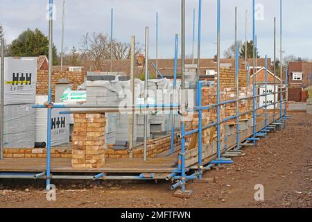 Vorderecke der neuen Ziegel- und Blockwände, die für neue freistehende Wohngrundgerüste gebaut werden Baumaterialien gestapelt in England Stockfoto