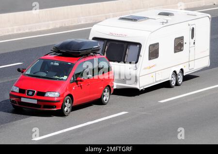 Fünftüriger roter Wagen der Marke SEAT mit schwarzem Dachgepäckträger, Abschleppen eines weißen Senator-Wohnwagens mit zwei Achsen auf der m25-Autobahn Essex England Großbritannien Stockfoto