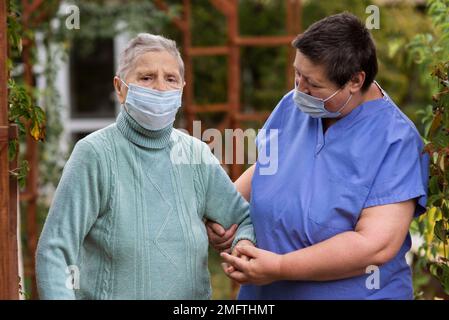 Krankenschwester kümmert sich ältere Frau mit medizinischer Maske Stockfoto