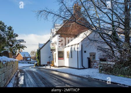 Blick auf die schneebedeckte St. Mary's Parish Church in Astbury in der Nähe von Congleton Cheshire England des Egerton Arms Public House im Winterschnee Stockfoto